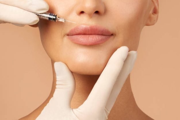 istockphoto-2157259538-612×612 Lip injections concept. Young lady getting beauty injection in her lips, beautician holding syringe with filler next to woman mouth, cropped